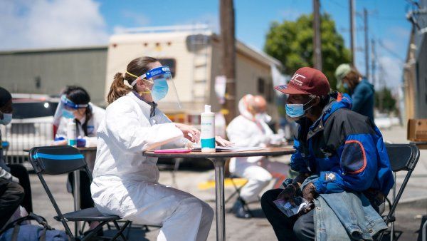 Clinician in PPE talks to unhoused man at an outdoor table