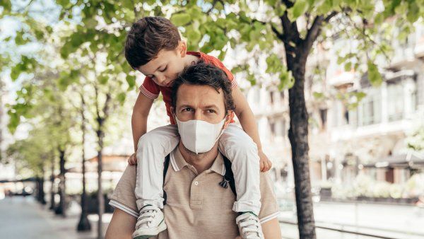Father wearing face mask with young son on this shoulders