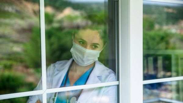 Doctor wearing mask leaning against window