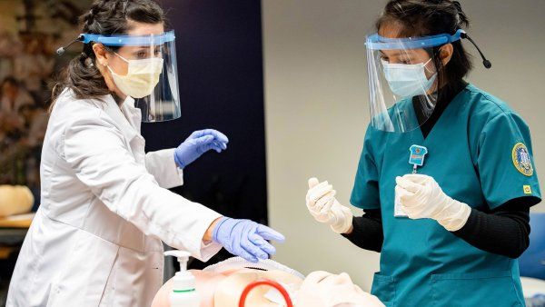 a nursing instructor points at a dummy while a student looks on