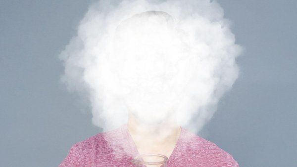 Photo of a person holding a large glass beaker, whose face is completely obscured with a smoke cloud.