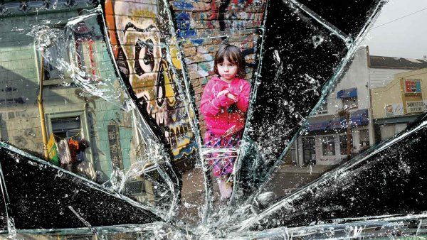 Photo collage with broken glass: run down buildings and a small child in front of a graffitied wall.