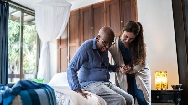 Home caregiver helping a black senior man standing up at home stock photo