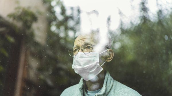 Senior man wearing mask looking through window