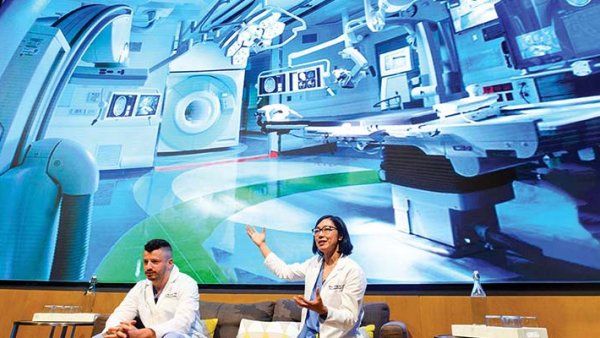 Two surgeons sit in front of a large screen, presenting an operating room of the future.
