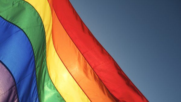 An LGBTQ rainbow flag against the sky