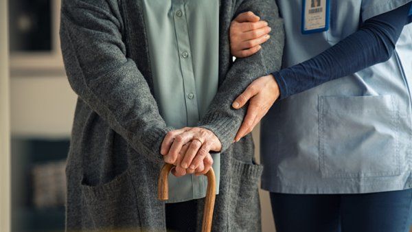 Nurse holds arm of elderly woman with a cane