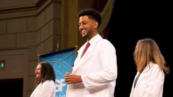 A medical student smiles as he stands onstage during a white coat ceremony