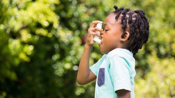 A young black boy uses an inhaler in a park
