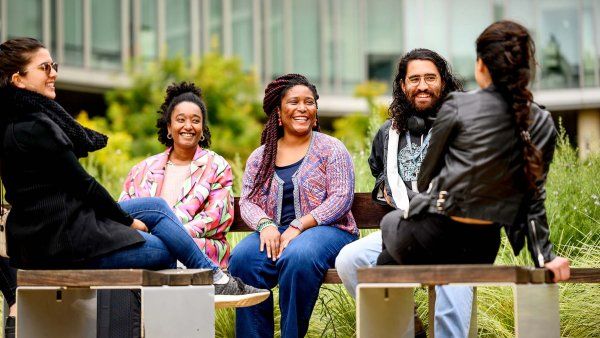 Several UCSFers sit outside on benches on the Mission Bay campus and laugh together