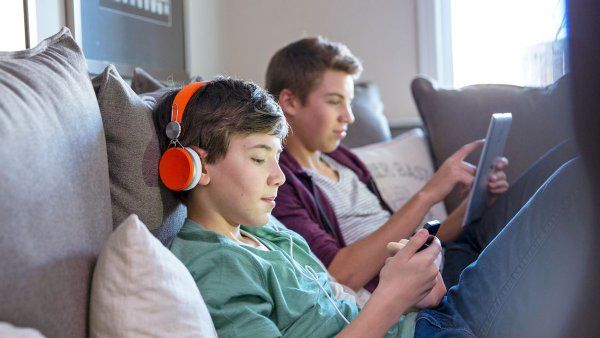 Two white teen boys with a digital tablet and smart phone sit on a sofa at home