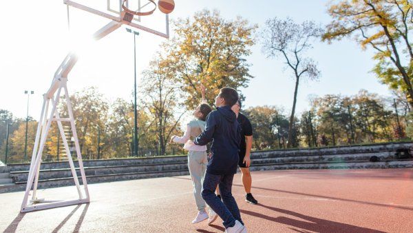 A young girl and boy play basketball with their father
