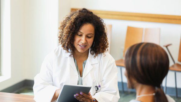 A Black female doctor holds a digital tablet as she consults with a female patient.