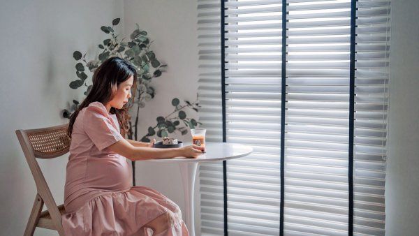 A pregnant woman sits at a table contemplating a dessert and a sugary drink.