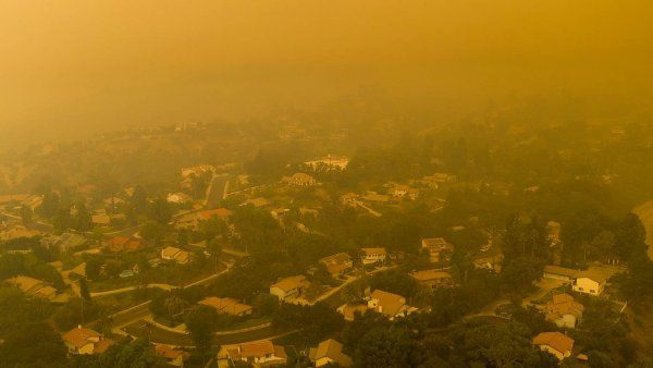 A haze of yellow smoke hangs over homes in a hilly residential neighborhood in California.