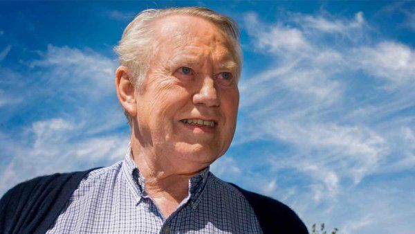 Chuck Feeney smiles as she stands under a blue sky.