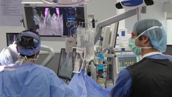 A surgeon looks at a screen with 3D imaging during a spine surgery.