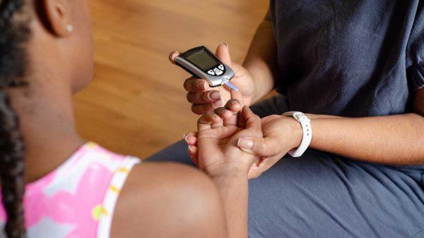 Mother measuring daughter's glucose with digital device.