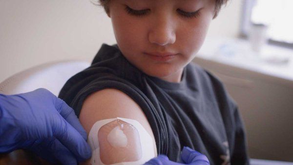 A medical professional places numbing cream on a young boy's arm before giving him an injection.