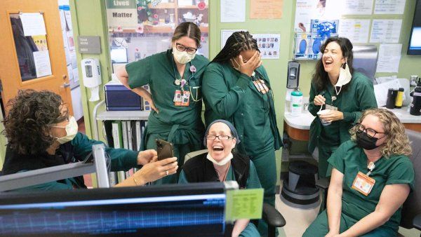 A group of nurses wearing green scrubs laugh together at the labor and delivery nurses station at ZSFGH.