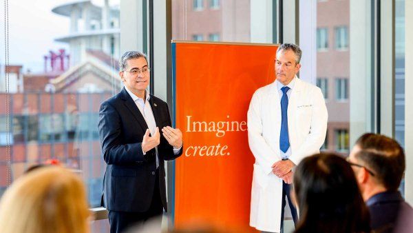 Xavier Becerra (left) speaks to a crowd in a light-filled atrium at Zuckerberg San Francisco General Hostpial. Daniel Grossman stands to his right. In the middle is a large orange banner with the UCSF expression that reads "Imagine. Create."