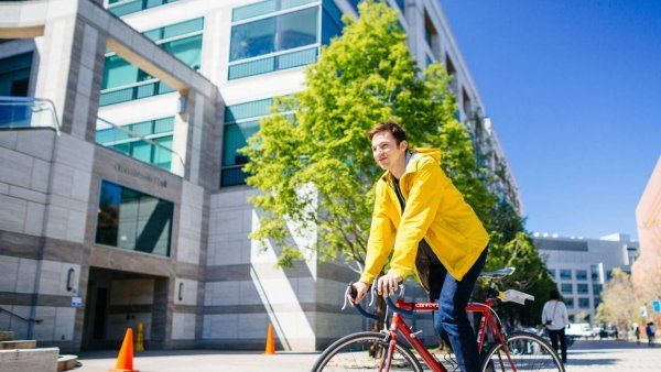 young man in yellow coat rides bike on campus