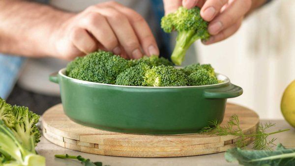 A man fixes broccoli onto a green plate.