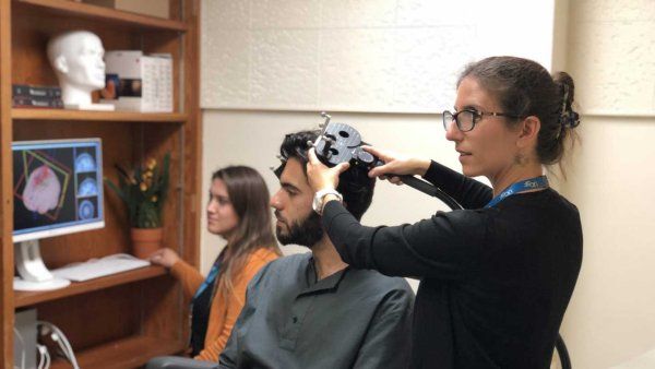 Psychiatrist Katherine Scangos adjusts a device over a man's head that is used for transcranial magnetic stimulation treatment.