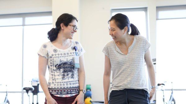 Two women smile at the gym and look at eachother.