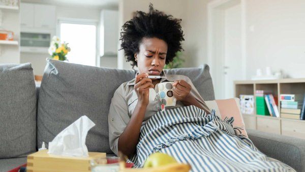A sick woman takes her temperature on her couch at home.