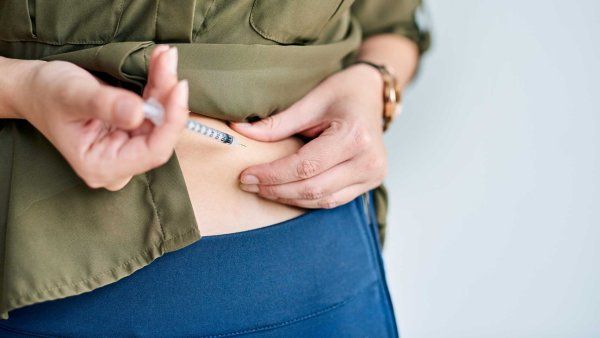A woman injects medication into her abdomen.