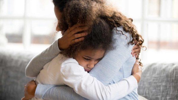 A mother holds her young daughter who shows signs of stress.