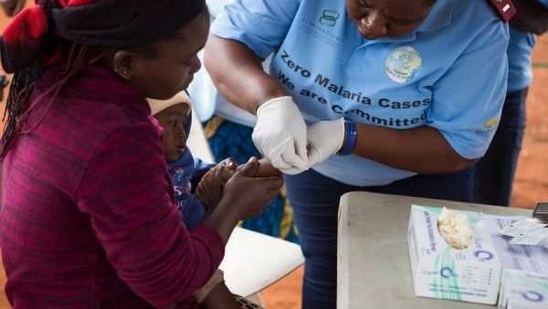 A mother holds her baby as a medical practicioner delivers a malaria vaccine.