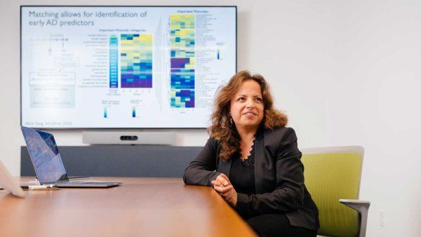 Marina Sirota, PhD, sits at a long conference table in front of a projection screen that shows visualization of research data.