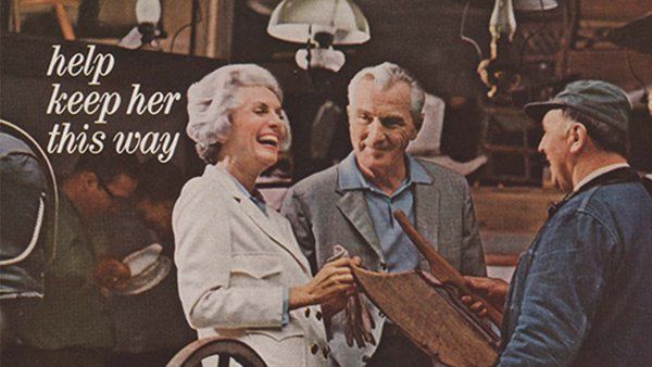 A vintage print advertisement. In a warmly lit workshop, an older white woman with gray hair, laughs and smiles while standing beside two older men who are examining a wooden object. The ad text reads, “help keep her this way,” suggesting happiness and vitality.