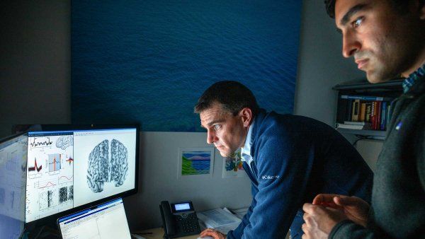 Researchers Jon Kleen and Alex Silva look at computer scrains showing a brain scan, graphic data, and scripting.