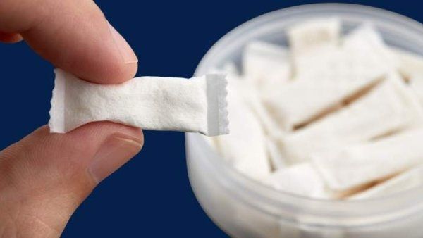 Close-up of a person's hand holding a small, white nicotine pouch between their thumb and index finger.