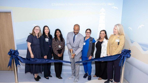 Nicholas Holmes cuts a blue ceremonial ribbon alongside clinicians and staff to celebrate the opening of the Children's Neuroscience Specialty Unit.