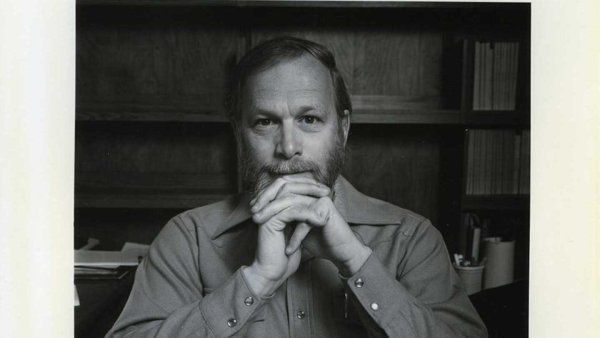 A black and white polaroid of J. Michael Bishop sitting at his desk.