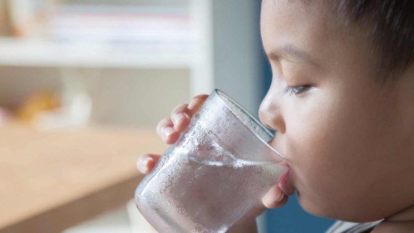 A young boy in toddler age drinks water from a glass.