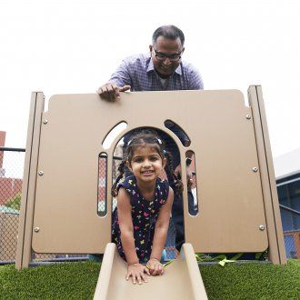 A little girl preparing to go down a slide with her dad watching