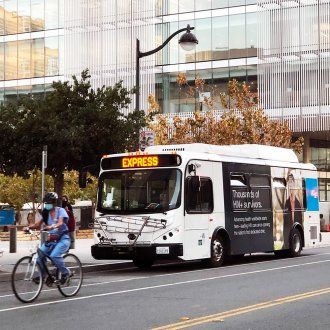 A bicyclist rides along the road with a parking shuttle parked behind