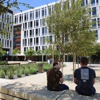 Two people sit in the Mission Hall courtyard surrounded by trees