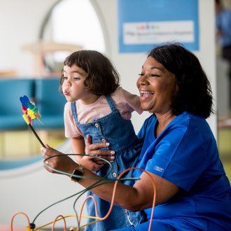 Nancy Pope holds a child patient while she blows on a handheld windmill