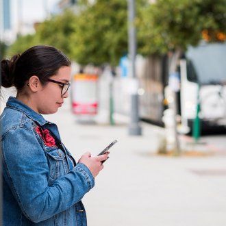 A woman looks at her phone while waiting for her shuttle with a bus in the background