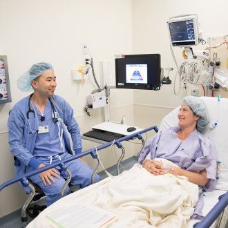 A patient lies down in a hospital bed prior to surgery and chats with her nurse anesthetist