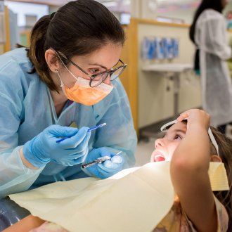 A dentist examines a little girl wearing a paper bib