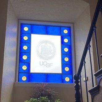 A blue and white stained glass window in the stairway that has the UCSF seal