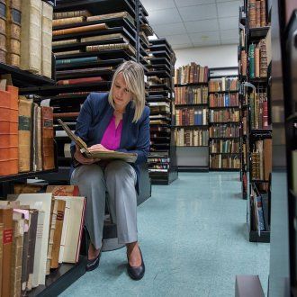 Archivist Polina Ilieva sits among rows of shelves containing historical books and documents