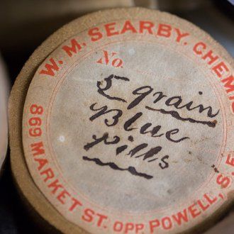 The cap of an old pill bottle that reads 5 grain blue pills in handwritten ink